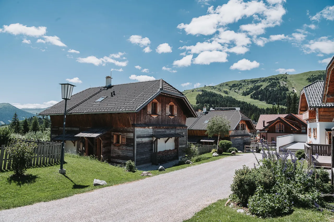 Weg zwischen den Almchalets im Sommer, hinten der grüne Skihang