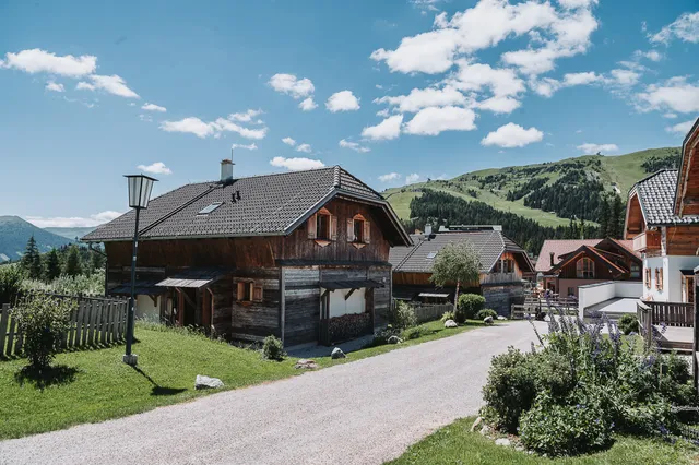 Weg zwischen den Almchalets im Sommer, hinten der grüne Skihang