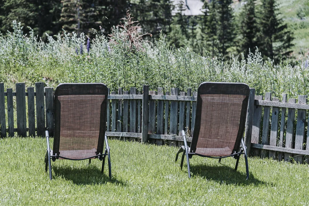 Zwei Liegestühle im eingezäunten Garten, dahinter Wald und Berge