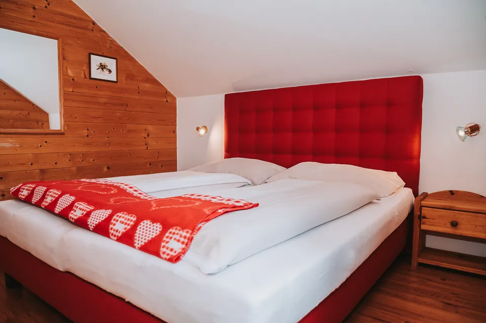 Schlafzimmer mit rotem Kopfteil und Holzwand im Almchalet