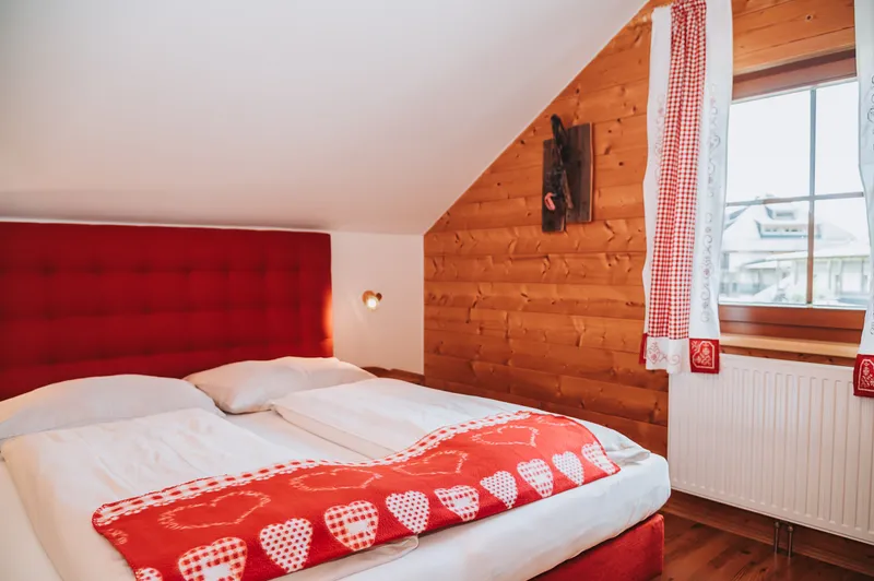 Doppelbett mit rotem Kopfteil unter der Dachschräge, daneben ein Fenster