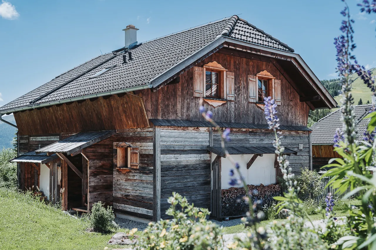 Almchalet aus dunklem Holz mit Blumen im Sommer