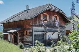 Almchalet aus dunklem Holz mit Blumen im Sommer