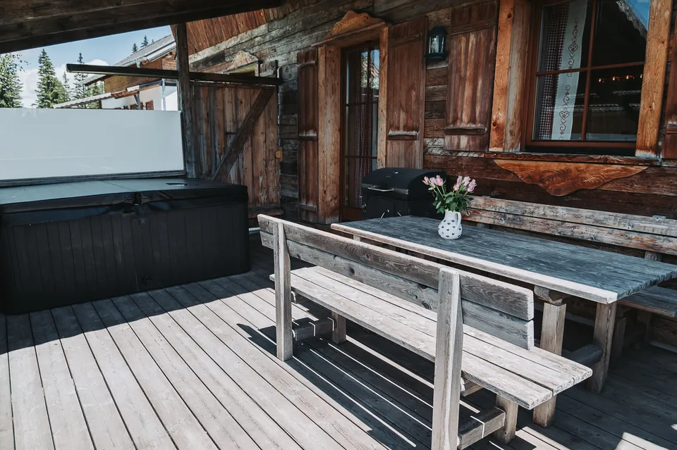 Überdachte Terrasse des Almchalets mit abgedecktem Whirlpool, Holztisch und Bank