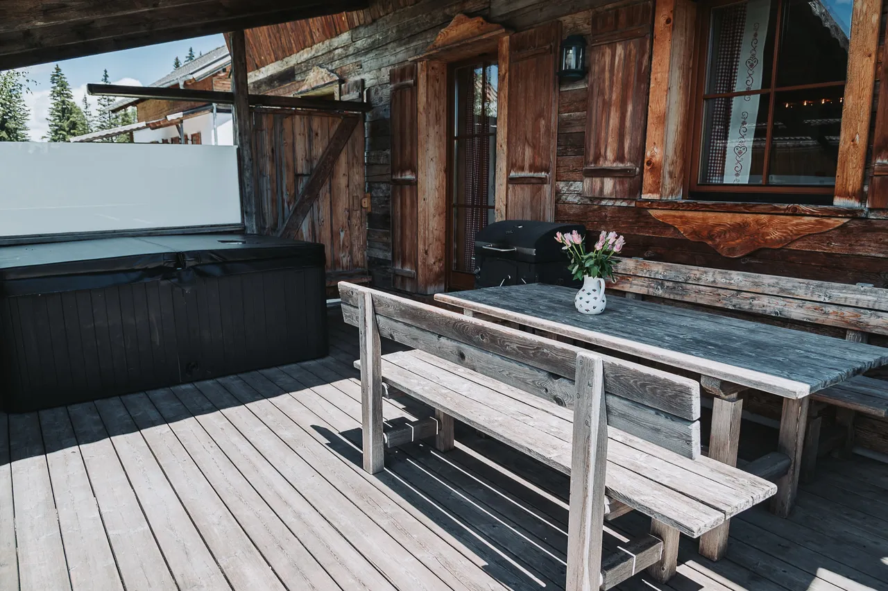 Überdachte Terrasse des Almchalets mit abgedecktem Whirlpool, Holztisch und Bank