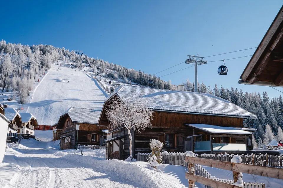 Verschneite Almchalets am Katschberg, dahinter die Skipiste und die Gondelbahn