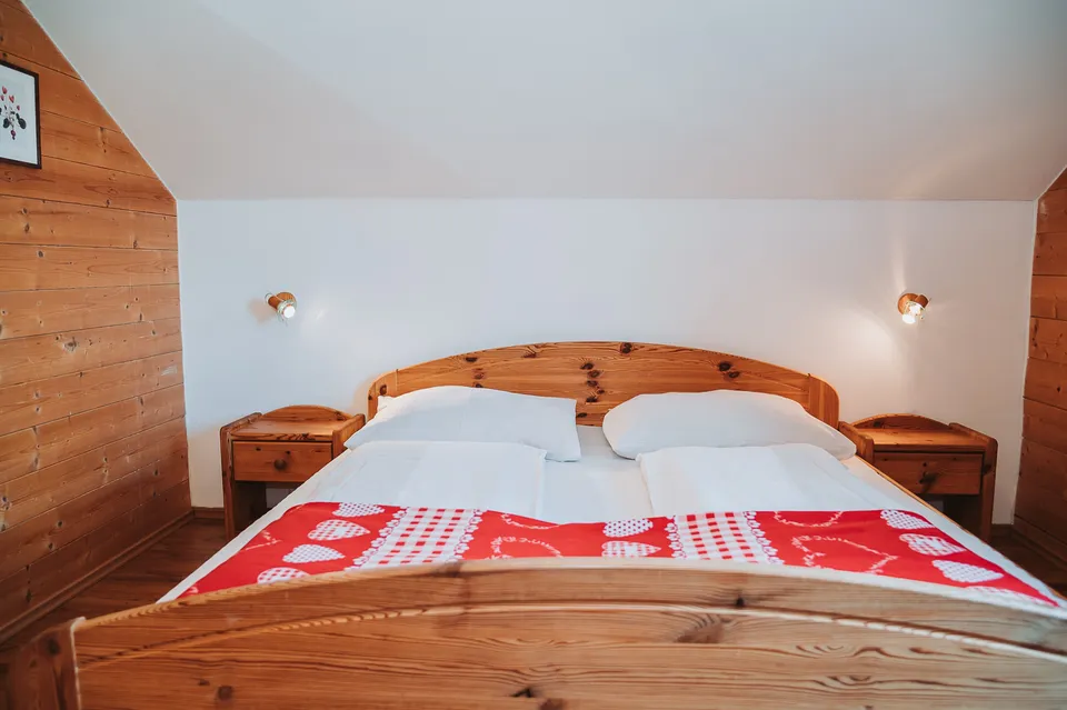 Schlafzimmer mit Holzbett und roter Decke in der Almhütte