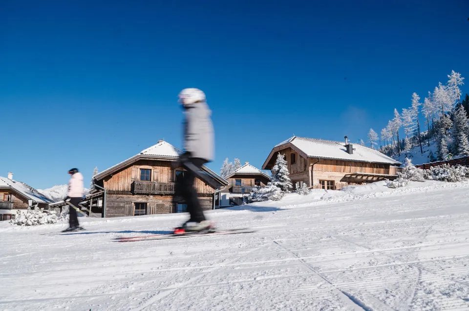 Skifahrer auf der Piste direkt an den verschneiten Almhütten