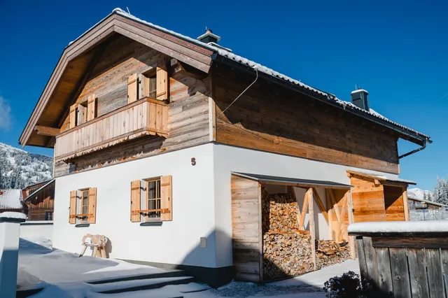 Verschneite Almhütte mit Holzbalkon und Fensterläden unter blauem Himmel