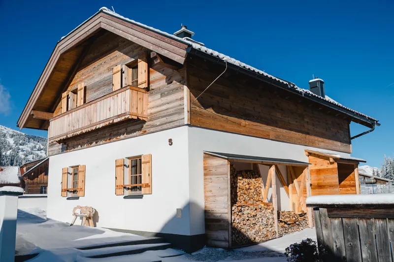Verschneite Almhütte mit Holzbalkon und Fensterläden unter blauem Himmel