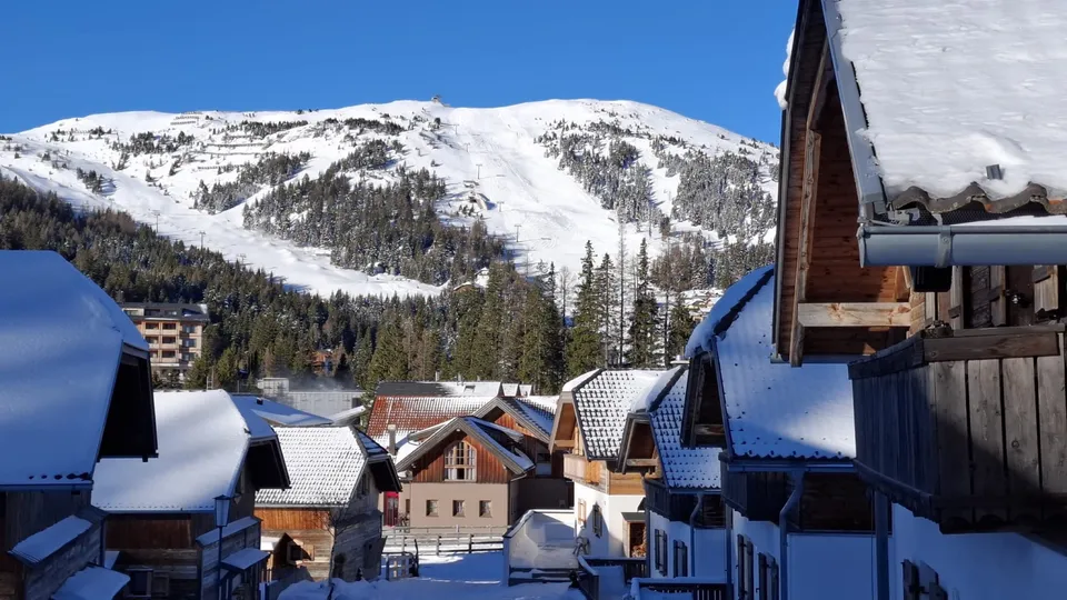Blick über verschneite Dächer auf das Skigebiet Katschberg