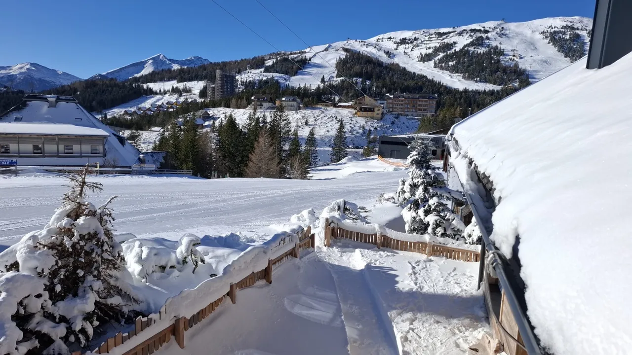 Verschneite Dächer des Almdorfs mit Blick auf das Skigebiet