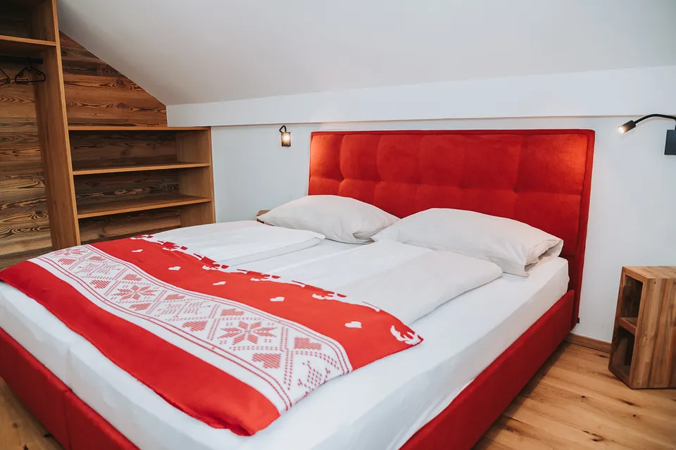Schlafzimmer mit rotem Bett unter der Dachschräge im Chalet Panorama