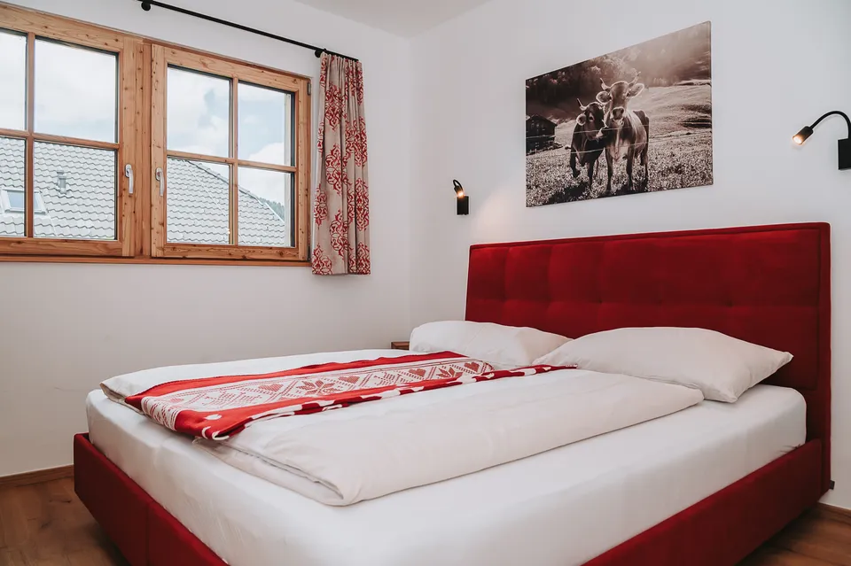 Doppelbett mit rotem Polsterkopfteil, darüber ein Bild mit Kühen